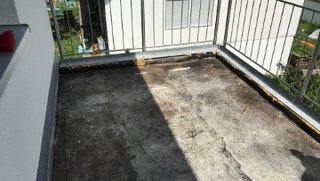 Verschlissene Balkonfläche mit rissigem Belag im Sonnenlicht