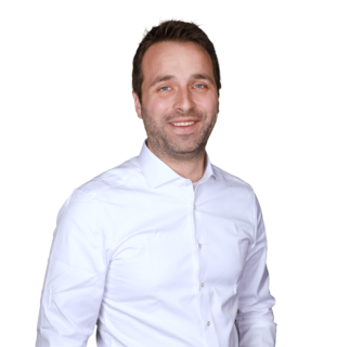 Porträt eines lächelnden Mannes in weißem Hemd vor neutralem Hintergrund